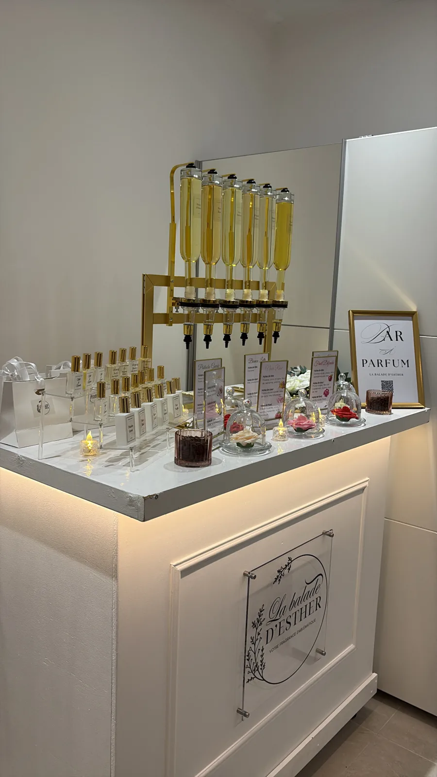 Le bar éclairé en intérieur, avec ses flacons, ses cartes de fragrances et l'enseigne La Balade d'Esther