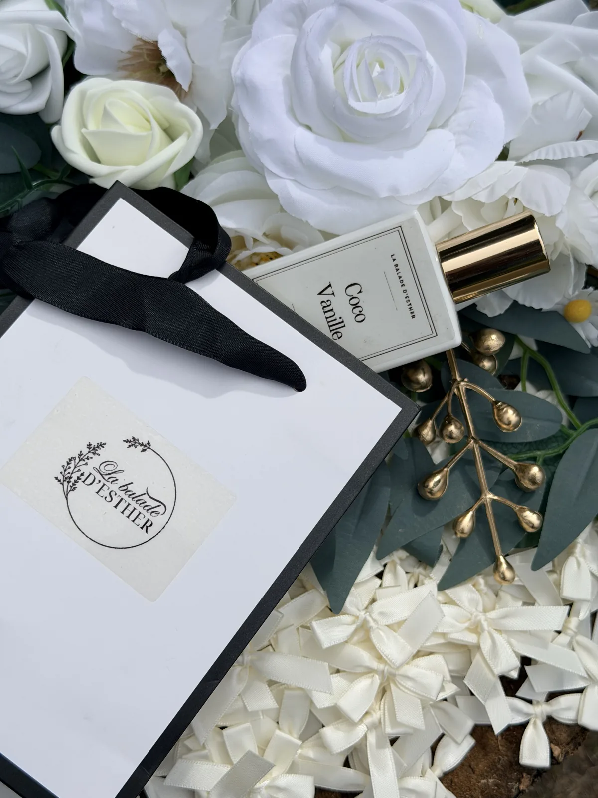 Flacon Coco Vanille et sac cadeau sur un lit de roses blanches et d'eucalyptus